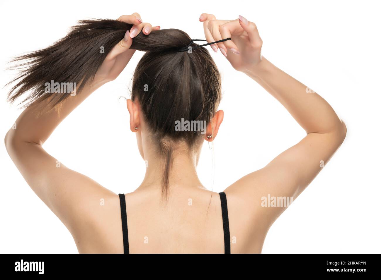 Rear view of a young woman tying her long hair on white background