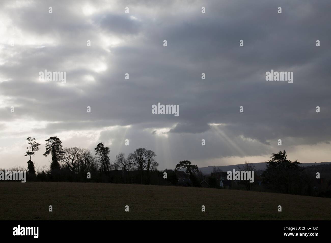 Winter sun's rays breaking through dark, stormy clouds onto fields and trees Stock Photo