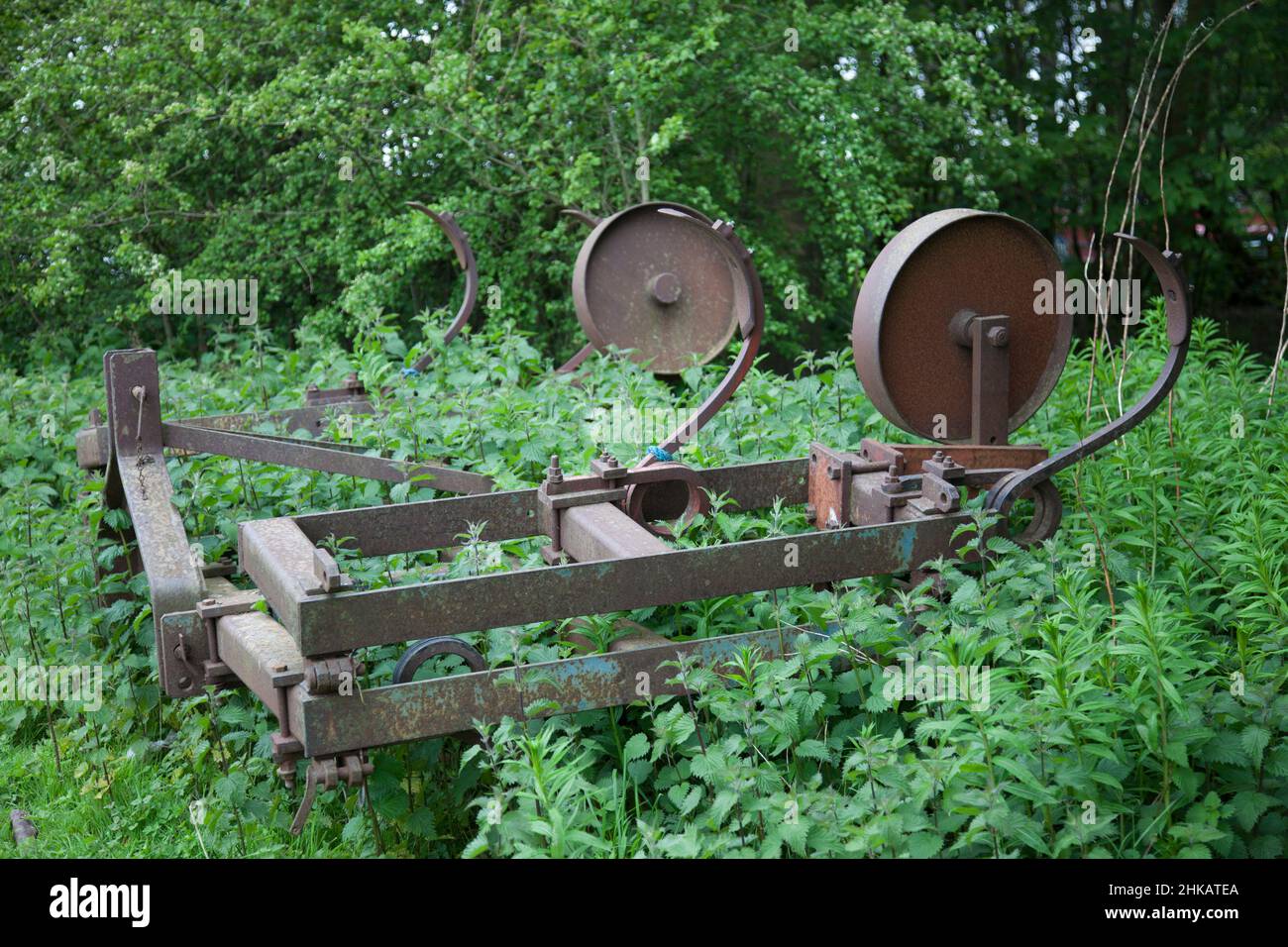 Abandoned farm tilling machinery left to rust in a field and now overgrown with weeds Stock Photo