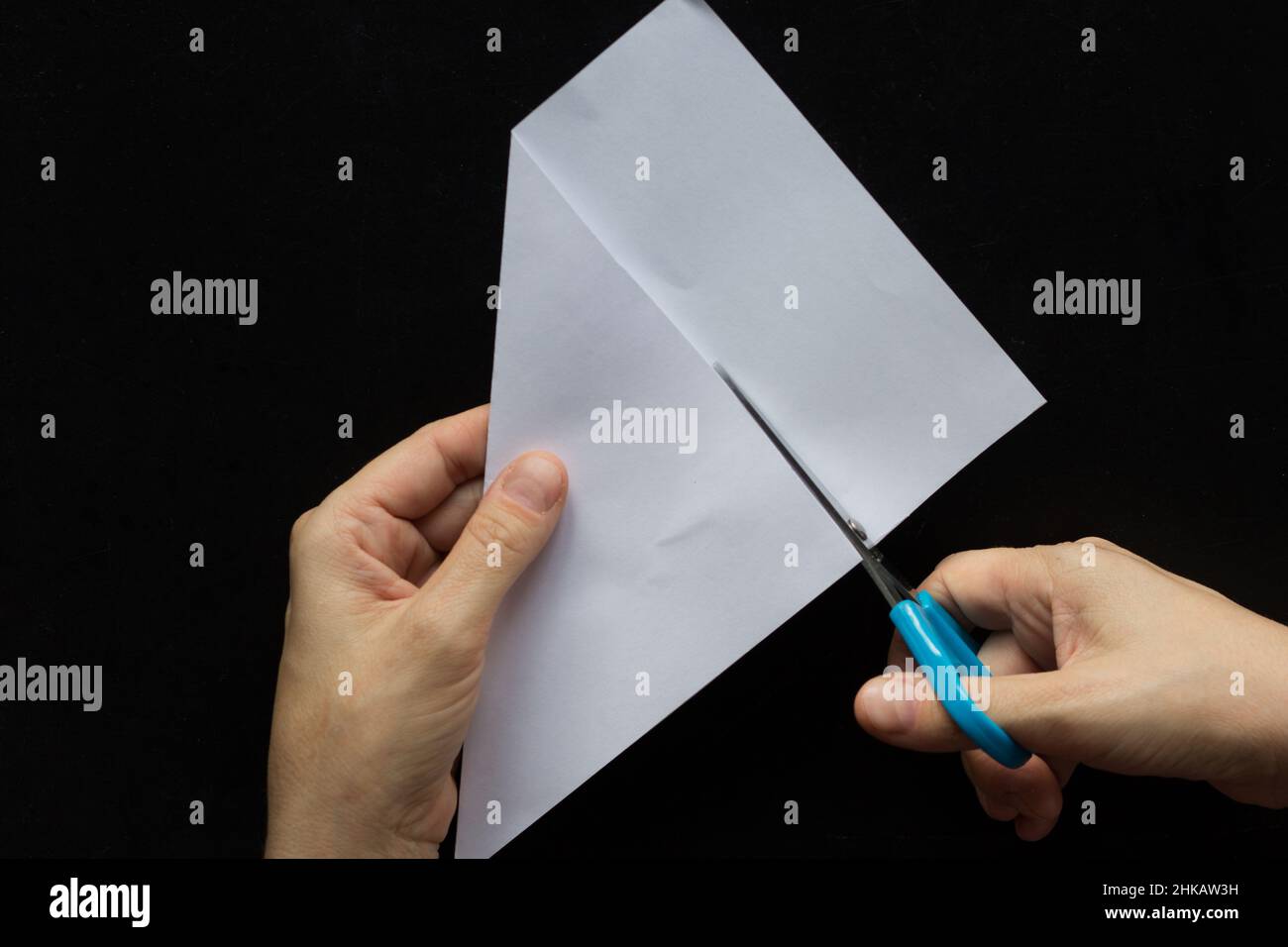Woman hands cutting away excess edge of paper to make it square on black background Stock Photo