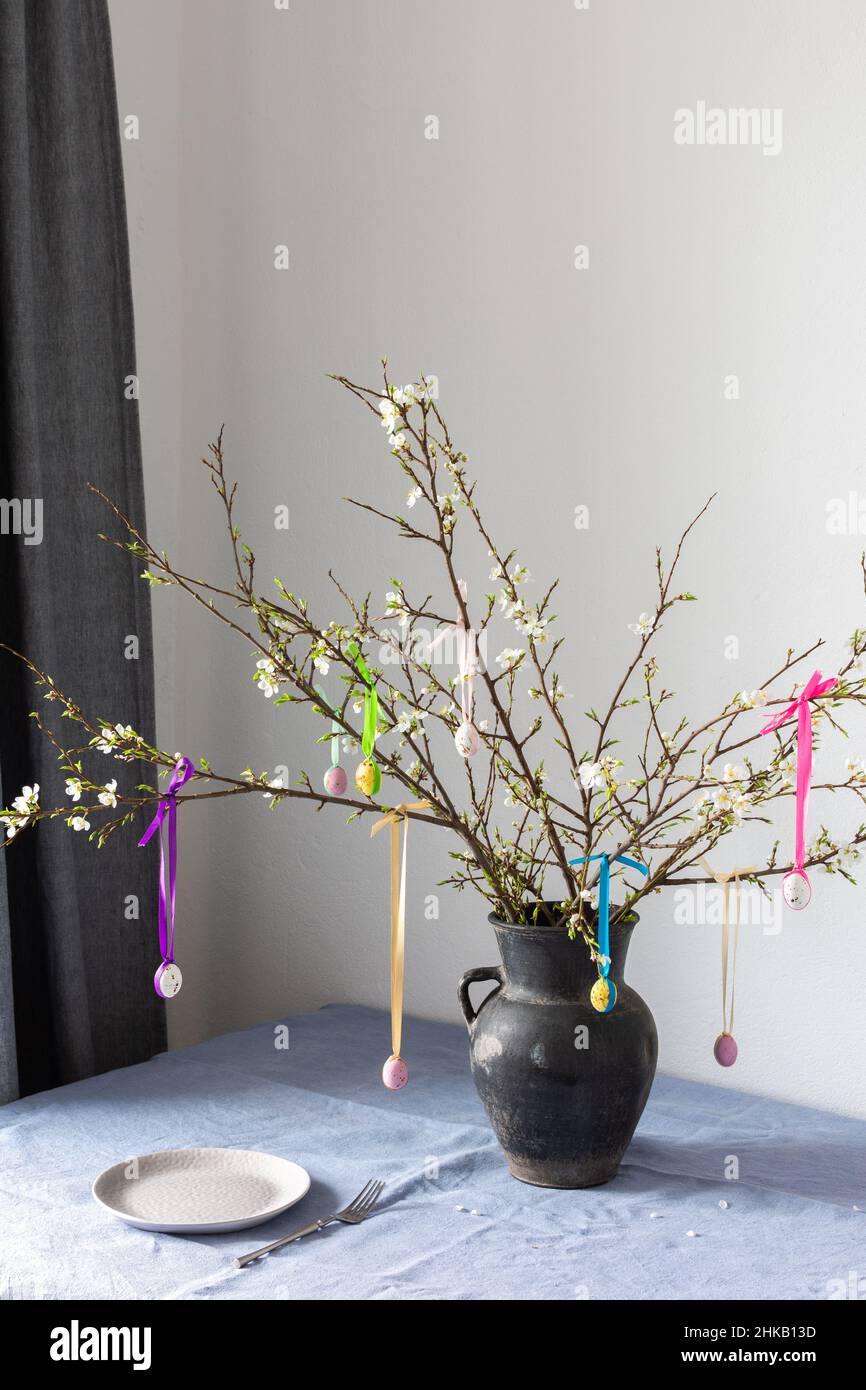 Blooming cherry branches decorated with colorful ribbons with Easter eggs, Happy Easter, table setting Stock Photo