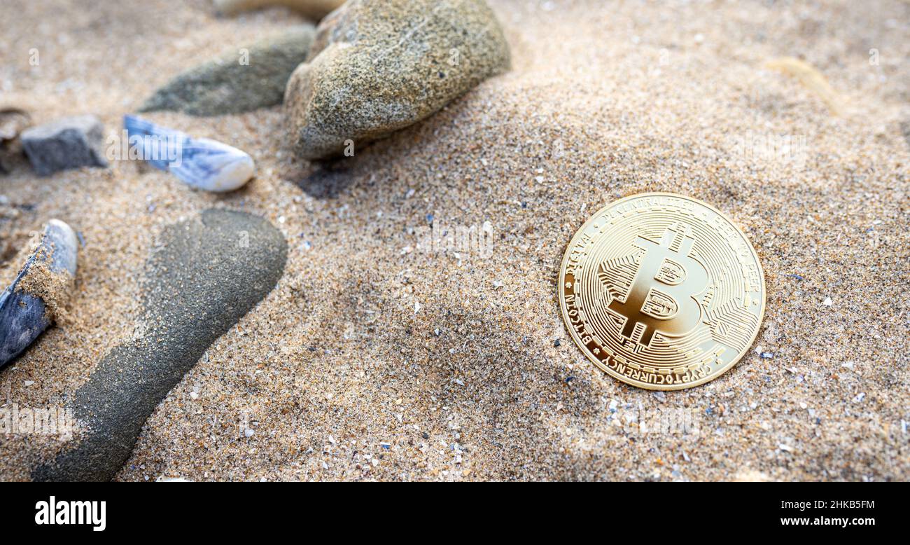 Bitcoin on the beach sand with shells and stones. Single golden BTC crypto coin banner with copy space for text top view. Environment impact of mining cryptocurrency concept. Stock Photo