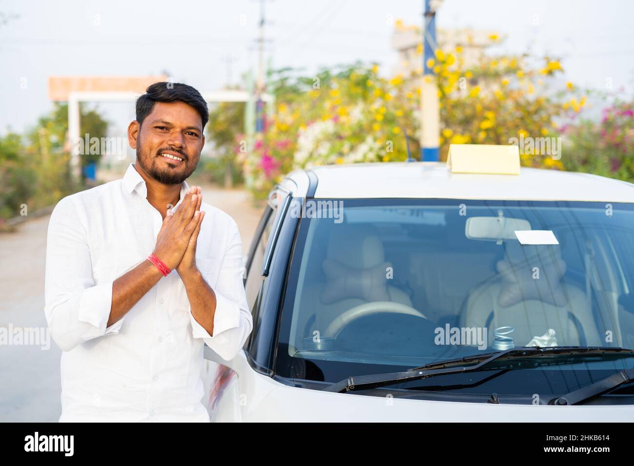 Happy smiling cab driver greeting by doing namaste in front of car by looking at camera - concept of welcoming passenger, transportation service and Stock Photo