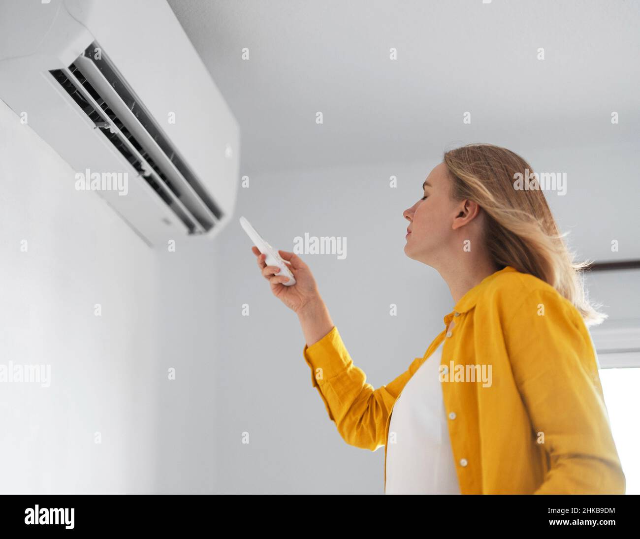 Women dying from the heat standing in front of the air conditioner. Stock Photo