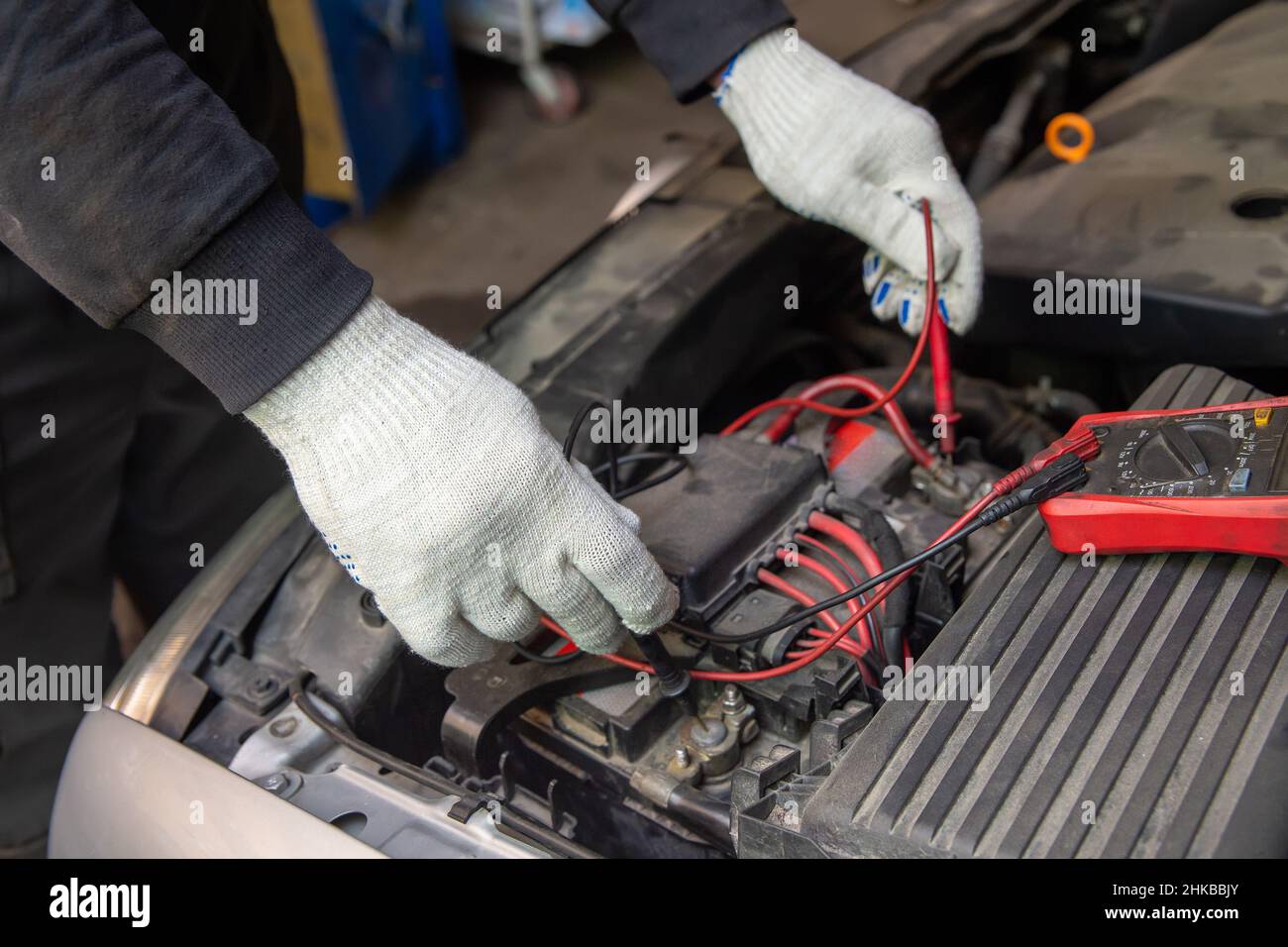 Selective focus an auto mechanic uses a multimeter voltmeter to check the voltage level in a car battery. Maintenance and repair. Stock Photo