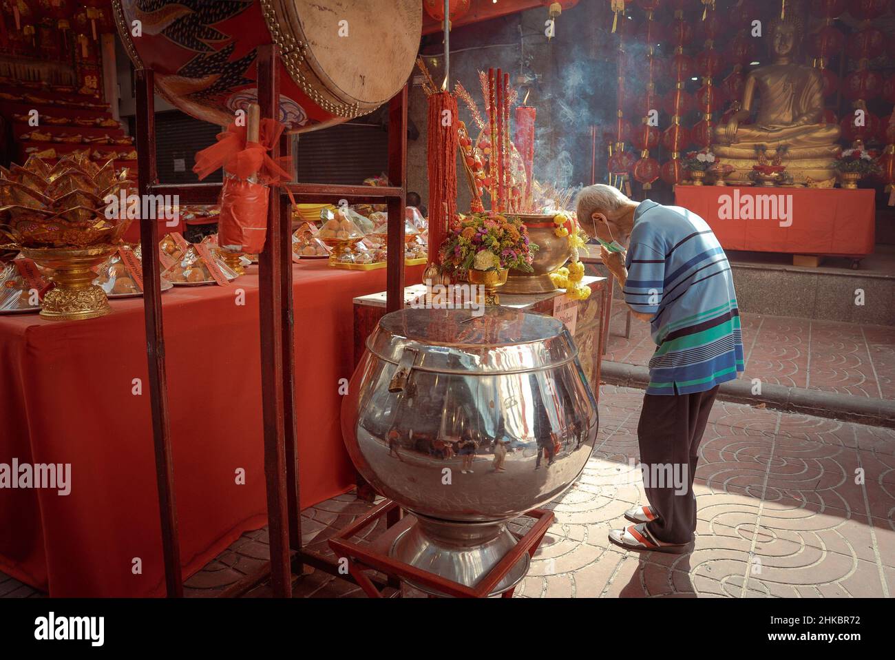 A man bows in prayer outside a shrine with offerings laid out.The Lunar New Year in Bangkok this year is a more solemn affair than in previous years. The government had technically canceled large celebrations, but in Chinatown, a troupe of lion dancers slowed down oncoming traffic on Yaowrat road. On a side street at Wat Lokanukroh, the only excitement for the day was the outbreak of a small fire caused when large lit red candles collapsed on one another; custodians rushed for a fire extinguisher. Many Thais of Chinese descent continued to perform rites and prayers at the shrine undisturbed. Stock Photo
