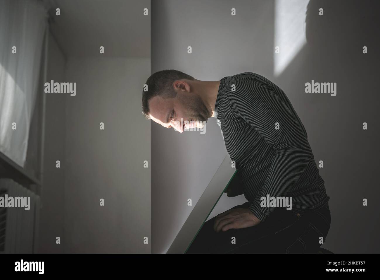 Conceptual profile portrait of young man looking in the mirror in a dark room Stock Photo