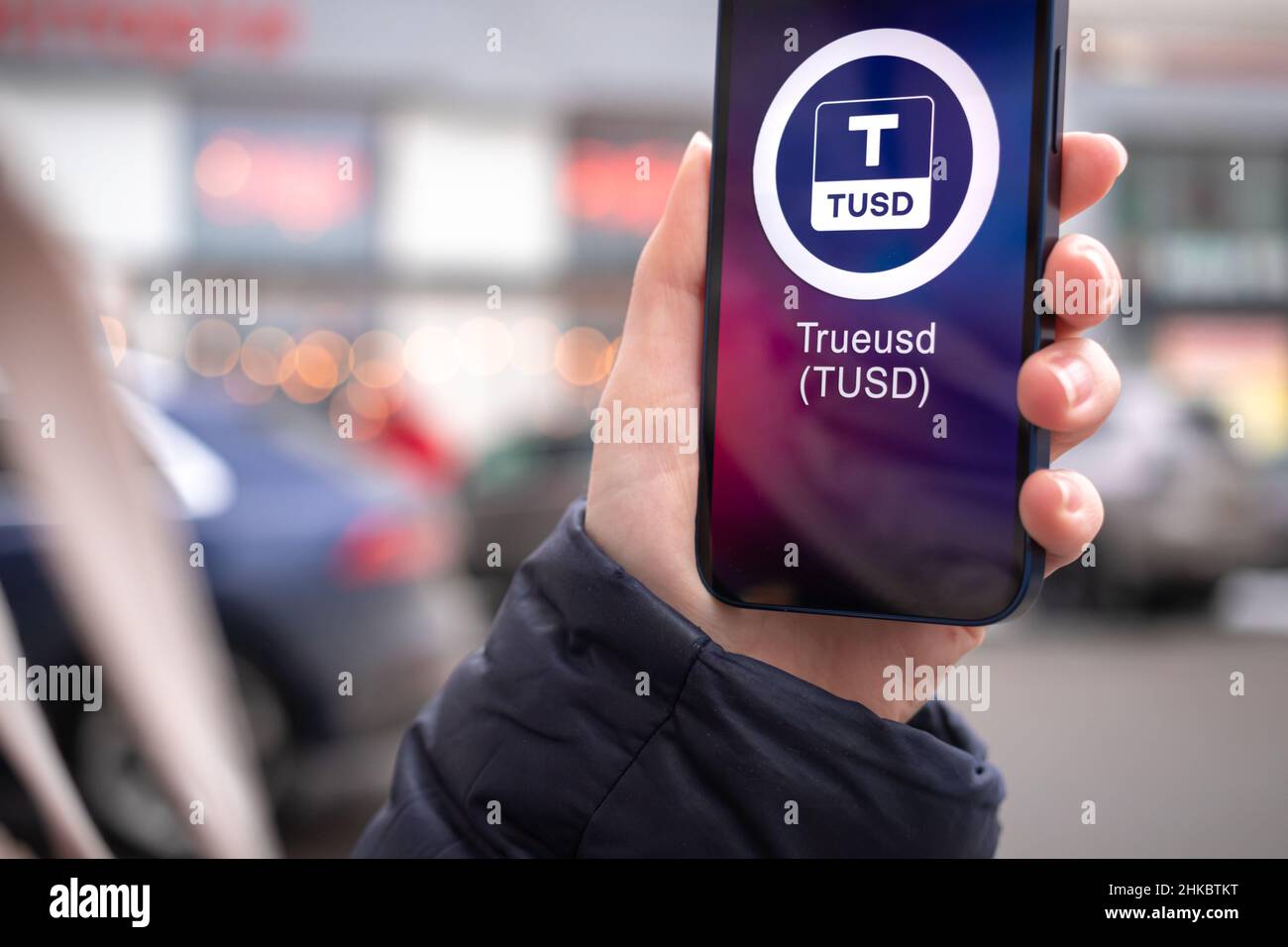 Kharkov, Ukraine - February 2, 2022: TrueUSD coin symbol. Trade with cryptocurrency, digital and virtual money, mobile banking. Hand with smartphone, Stock Photo
