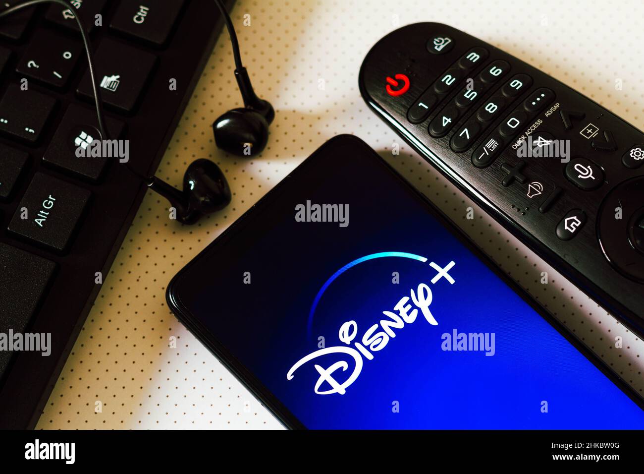 In this photo illustration, the logo of the Disney+ (Disney Plus), a subscription over-the-top video-on-demand streaming service seen displayed on a smart phone next a Tv remote control, earphones and a keyboard