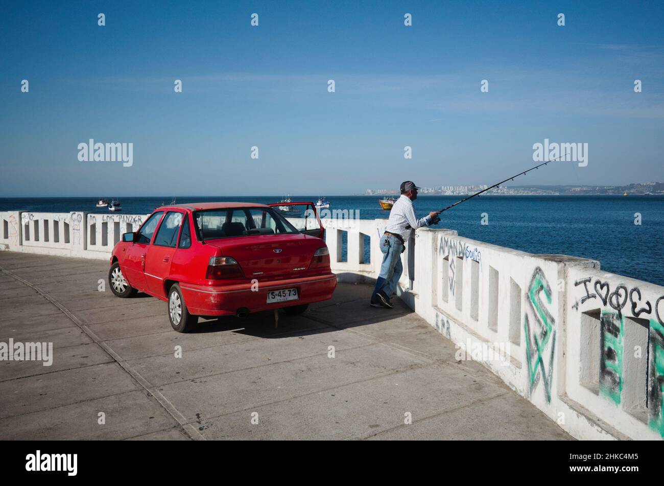 Valparaiso, Chile - February, 2020: Man with fishing rod is fishing on seafront of Valparaiso city. Red Daewoo car is parked on embankment Stock Photo