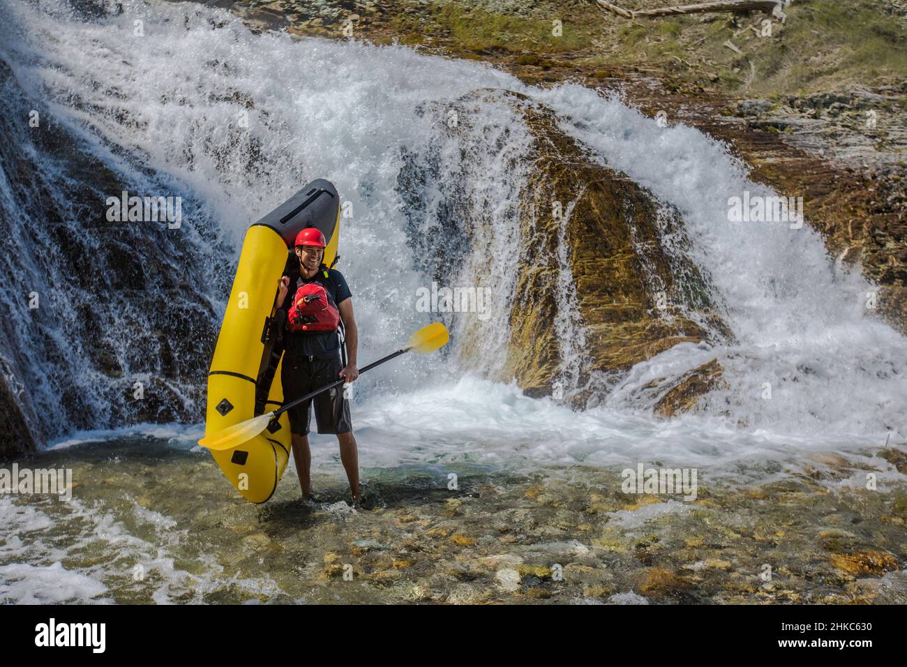 Man holds packraft in river next to waterfall. Stock Photo