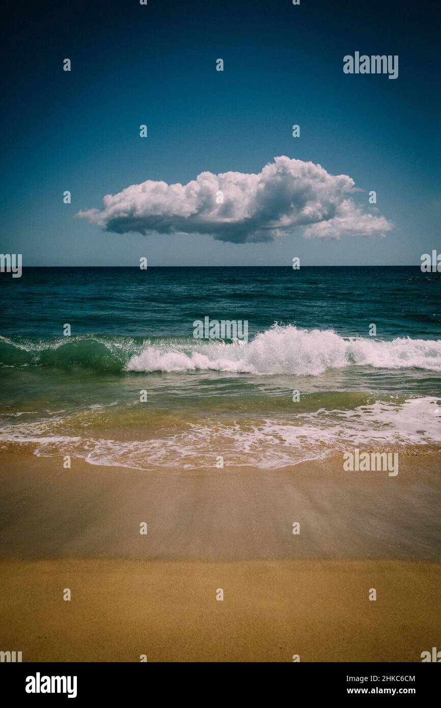 Lone Cloud Hovers over Blue Pacific waves and sand Stock Photo