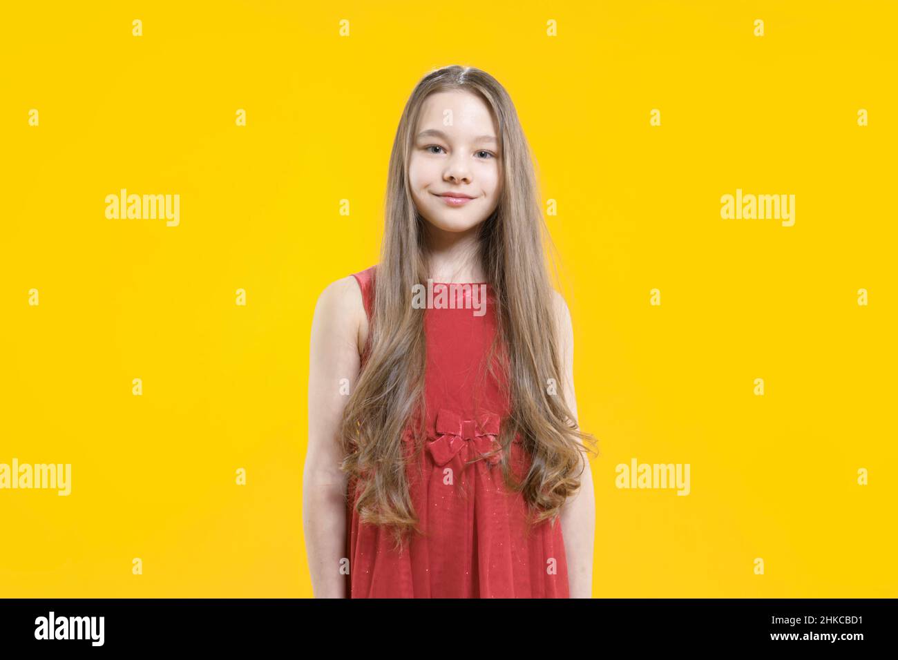 A cute teenage girl in a red dress with long blond hair stands on a ...