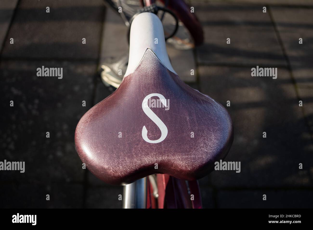 Classic bicycle seat, or saddle, burgundy and white, with the letter S on it, viewed from above. Stock Photo