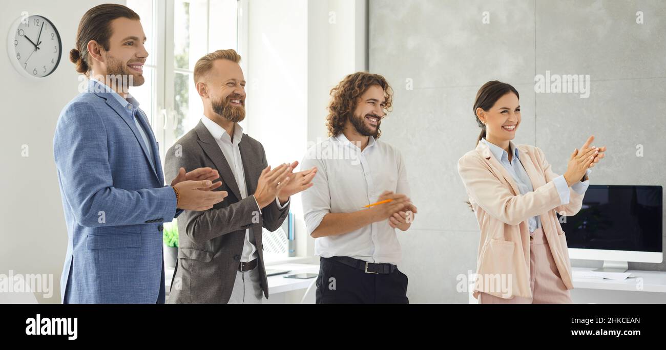 Group of happy business people standing in office, smiling and applauding someone Stock Photo