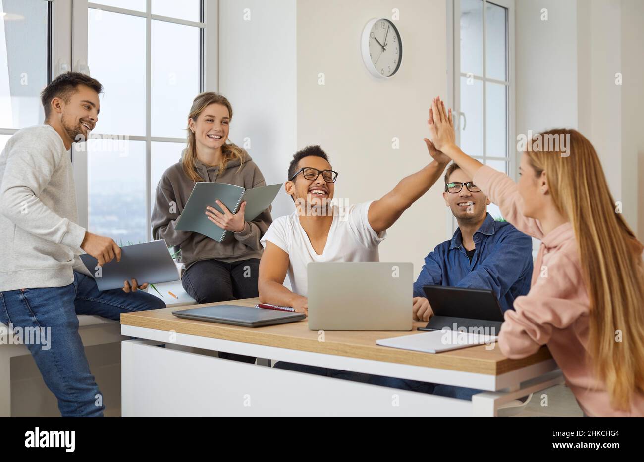 Cheerful multiracial students give each other five as they prepare for exam or lesson. Stock Photo