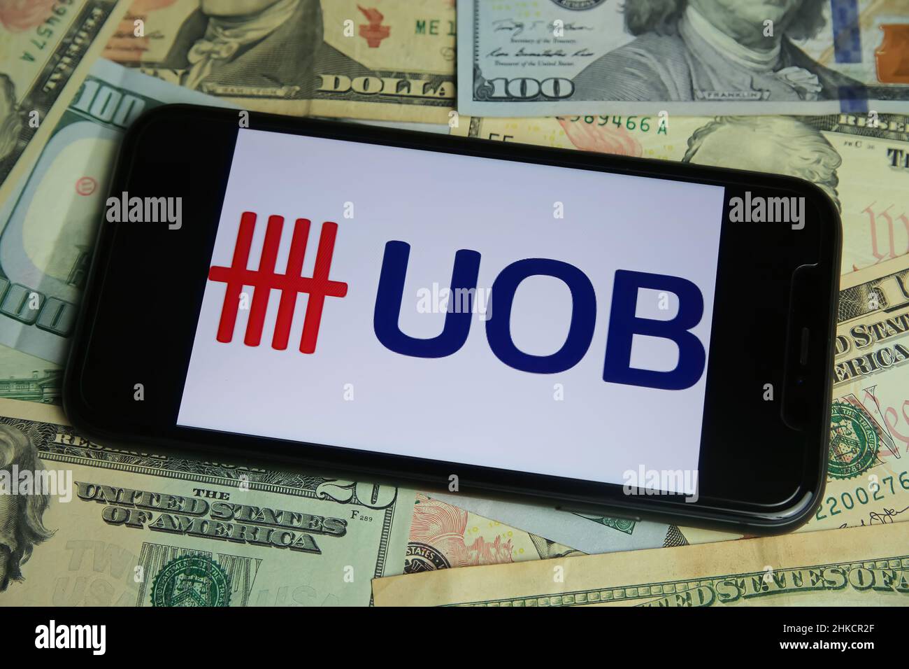 Viersen, Germany - January 9. 2022: Closeup of mobile phone with logo of united overseas bank UOB, us dollar paper banknotes background Stock Photo