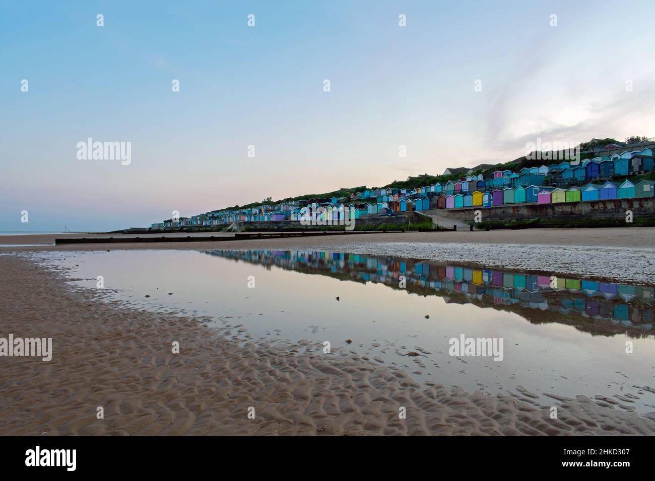 Colourful beach huts line the promenade of Walton-On-The-Naze, North Essex coastline, UK. Reflections created in pools left behind at low tide. Stock Photo