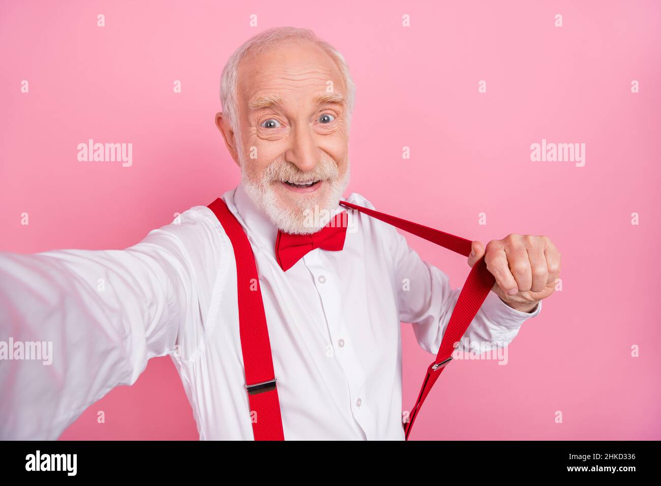 Self-portrait of attractive cheerful gray-haired man having fun pulling suspender isolated over pink pastel color background Stock Photo