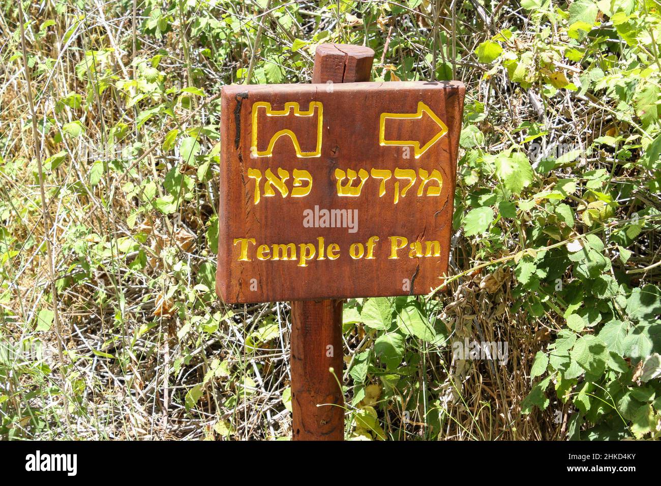 A brown wooden bilingual sign directs travelers to the Temple of Pan in the Herman Stream Banias Nature Reserve in the Golan Heights of Israel. Stock Photo