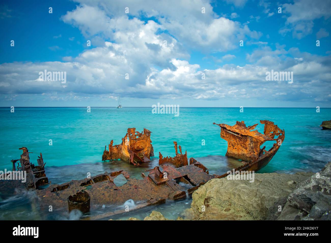 A sailing boat anchored in the light blue ocean behind The Gallant Lady shipwreck, North Bimini, Bahamas Stock Photo