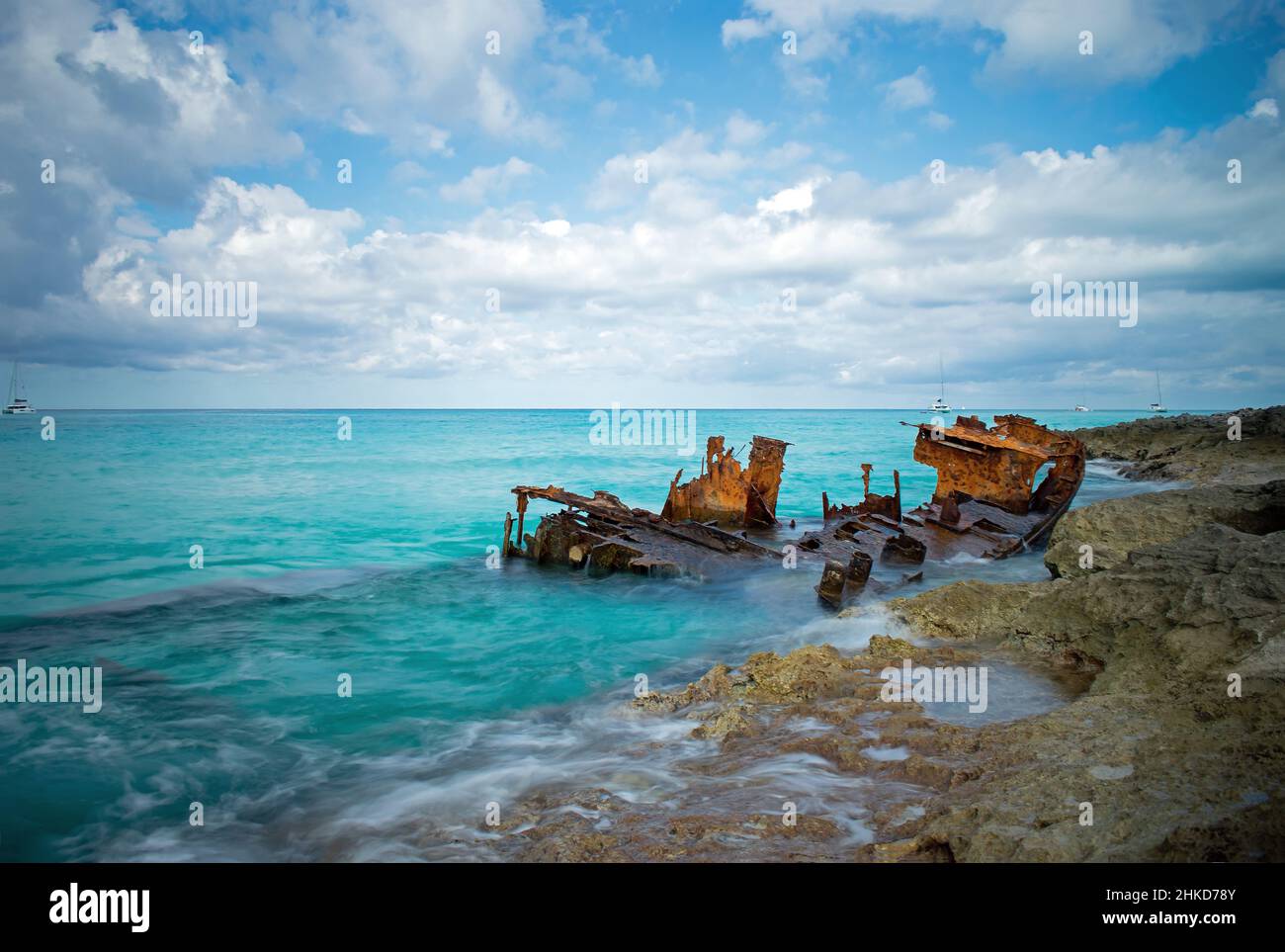 A rusting shipwreck of the Gallant Lady in the beautiful clear blue waters around North Bimini, Bahamas. Sailing boats are anchored in the distance. Stock Photo