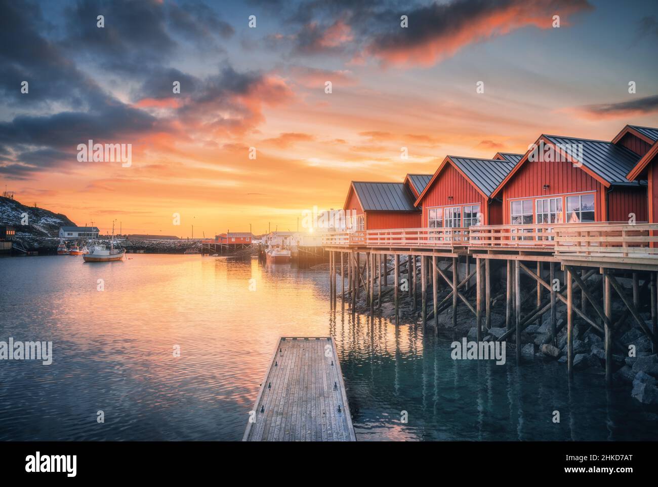 Red rorbu on wooden piles on sea coast, small jetty, orange sky Stock Photo