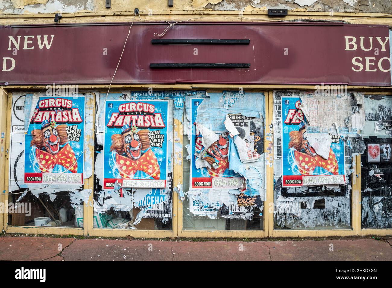 Closed shop. Boarded up former second hand store with ripped and torn circus advertising posters. Decaying building with bill stickers. Clown image Stock Photo