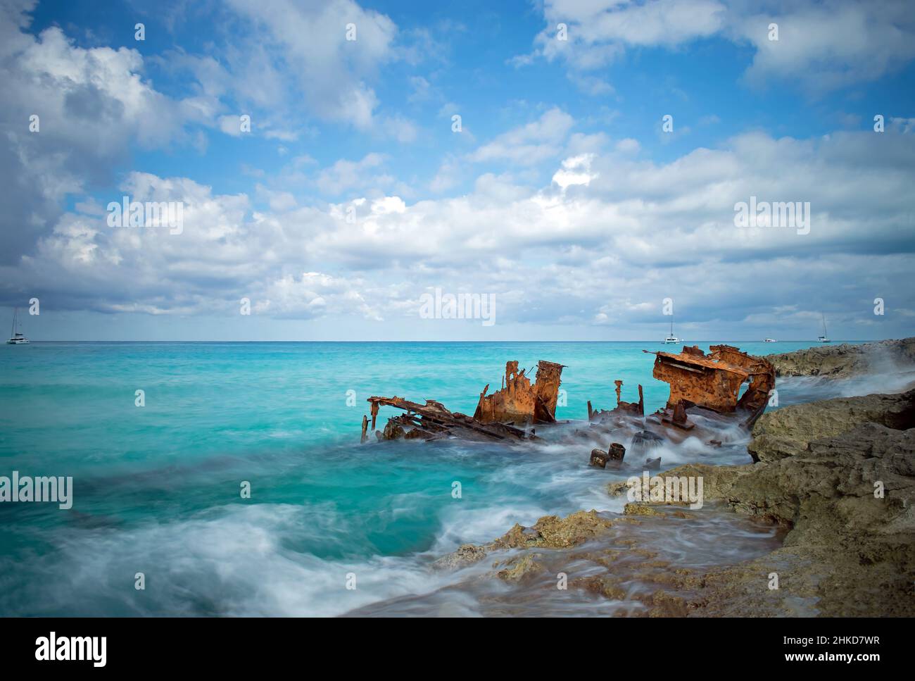 Waves break around the rusting hull of the Gallant Lady shipwreck on a cloudy day with blue sky, North Bimini, Bahamas Stock Photo