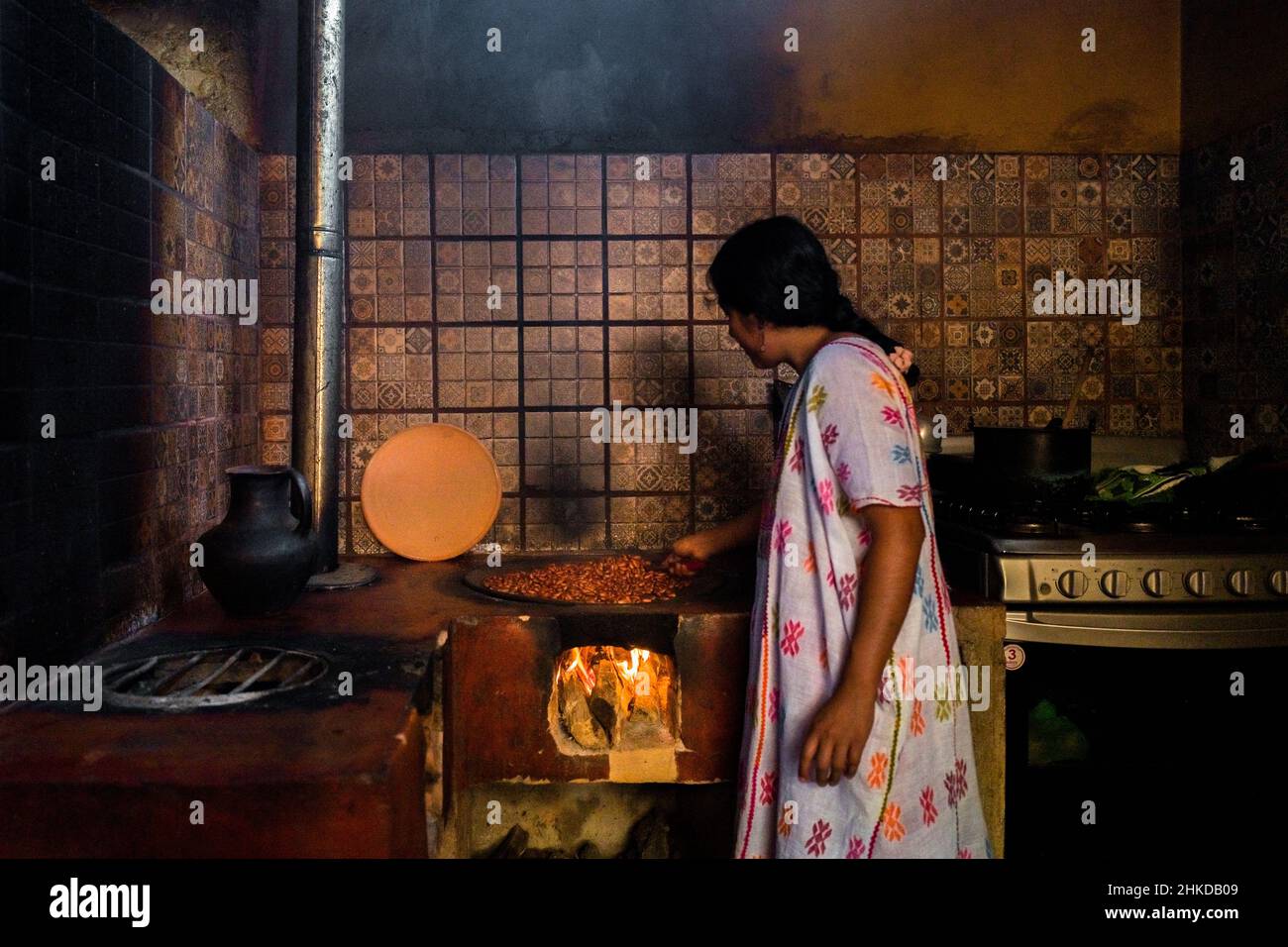 An Amuzgo indigenous woman roasts cacao beans on a clay plate over fire in artisanal chocolate manufacture in Xochistlahuaca, Mexico. Stock Photo