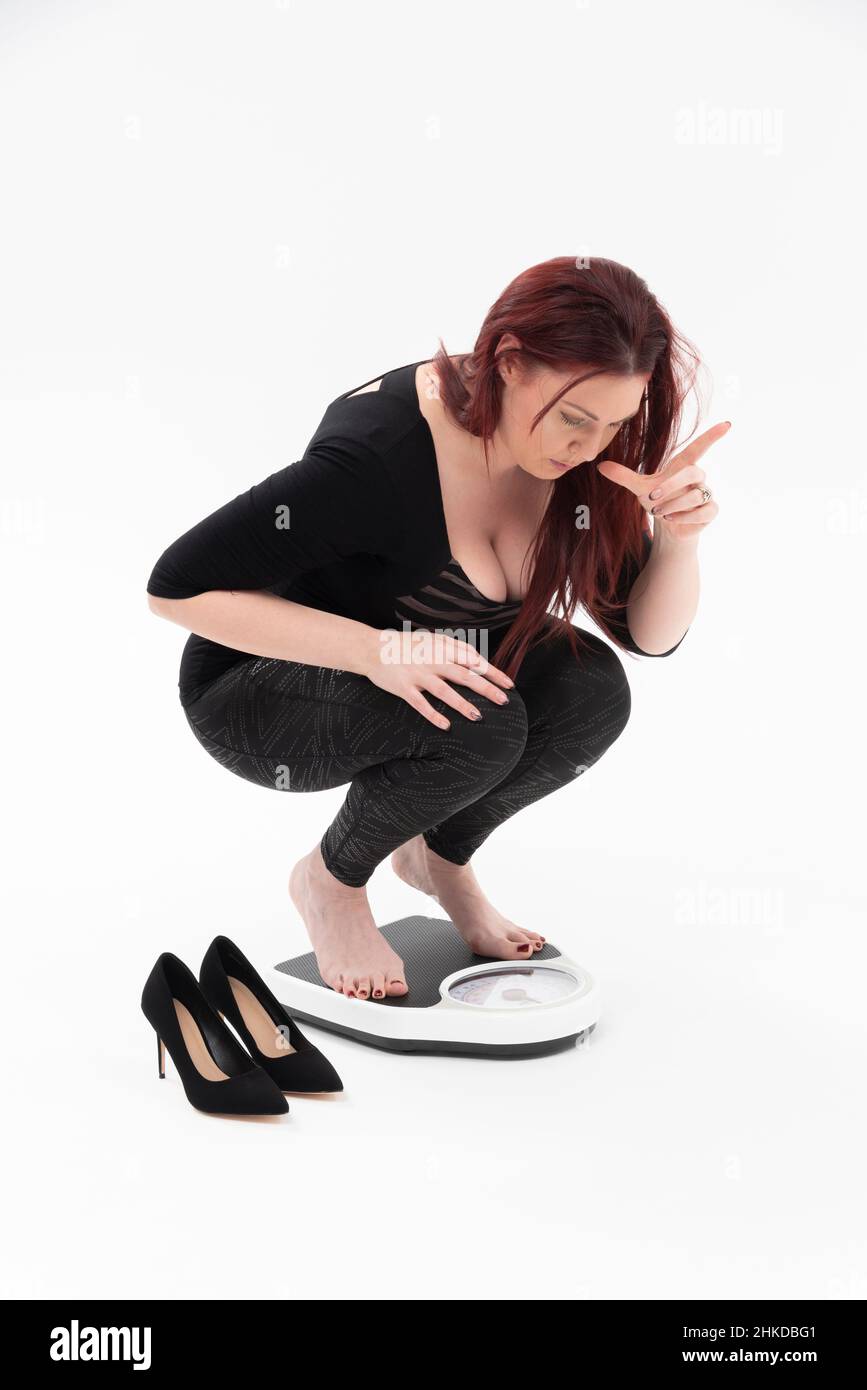 Wiltshire, UK. 2022.  Woman on bathroom scales checking her weight with white background. Stock Photo
