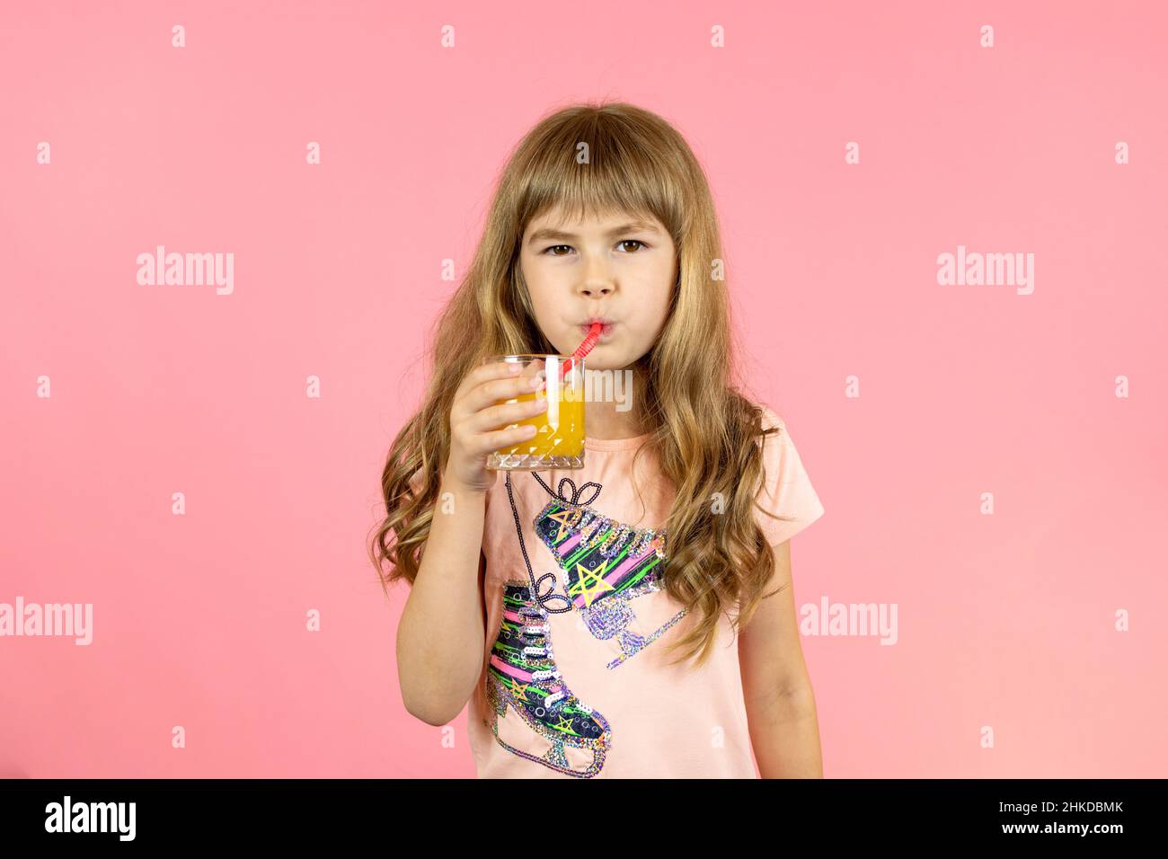 little girl drinks orange juice on a pink background Stock Photo Alamy