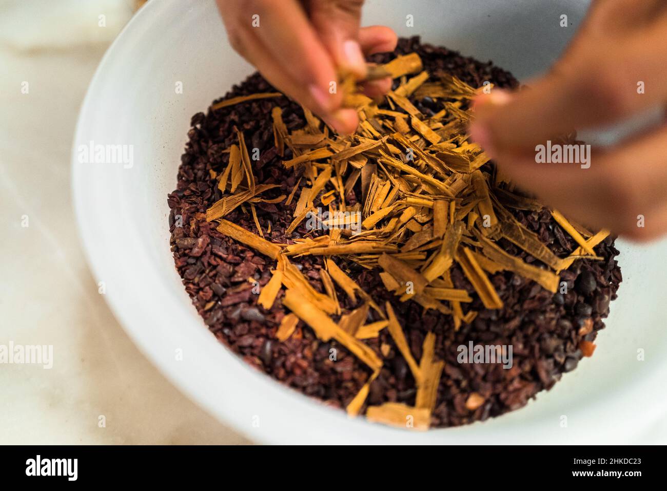 A Mexican man adds cinnamon into crushed cacao beans before the grinding process in artisanal chocolate manufacture in Xochistlahuaca, Mexico. Stock Photo