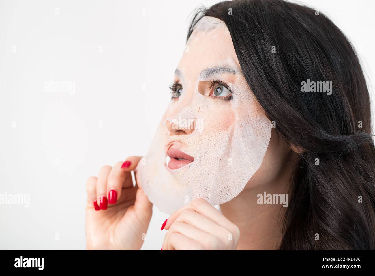 Face care and beauty treatments. Woman with a sheet moisturizing mask on her face isolated on white background. Stock Photo