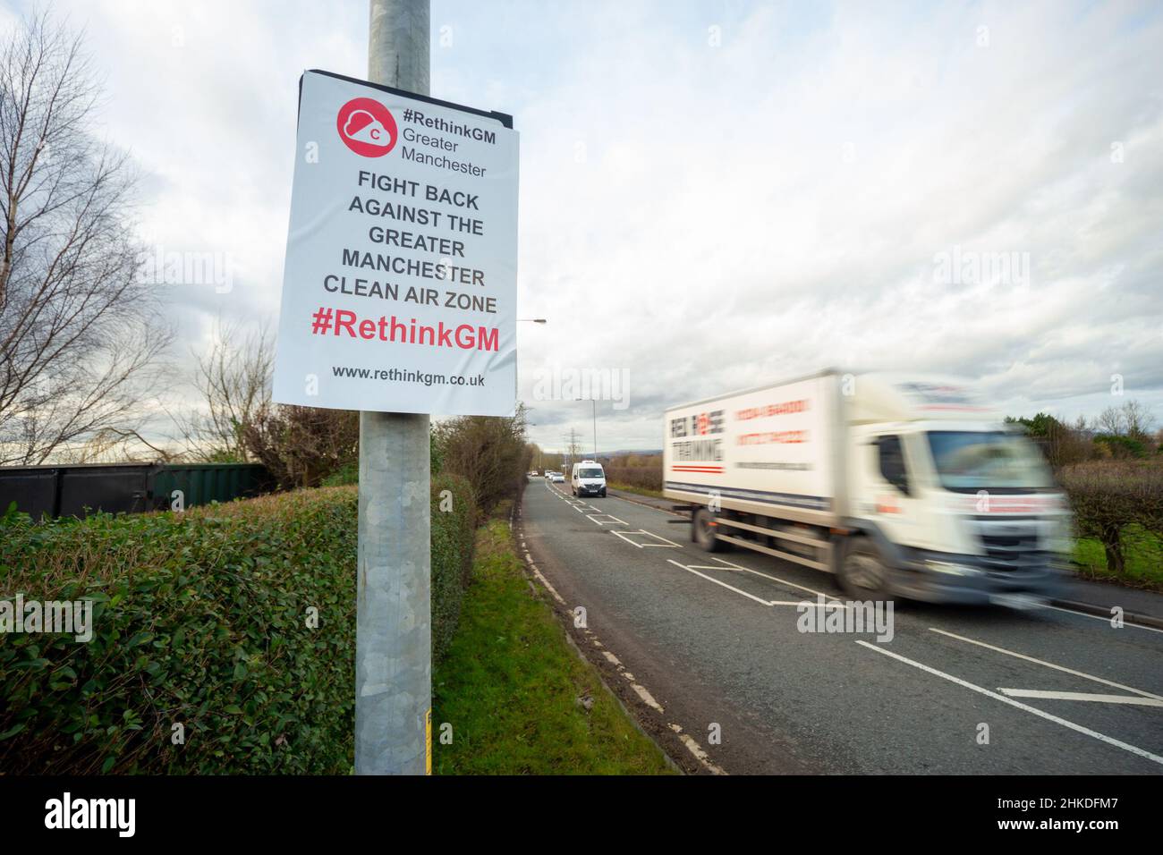 Commercial vehicles drive by a Clean Air Zone sign in Greater Manchester obscured with a poster in protest of the scheme Stock Photo
