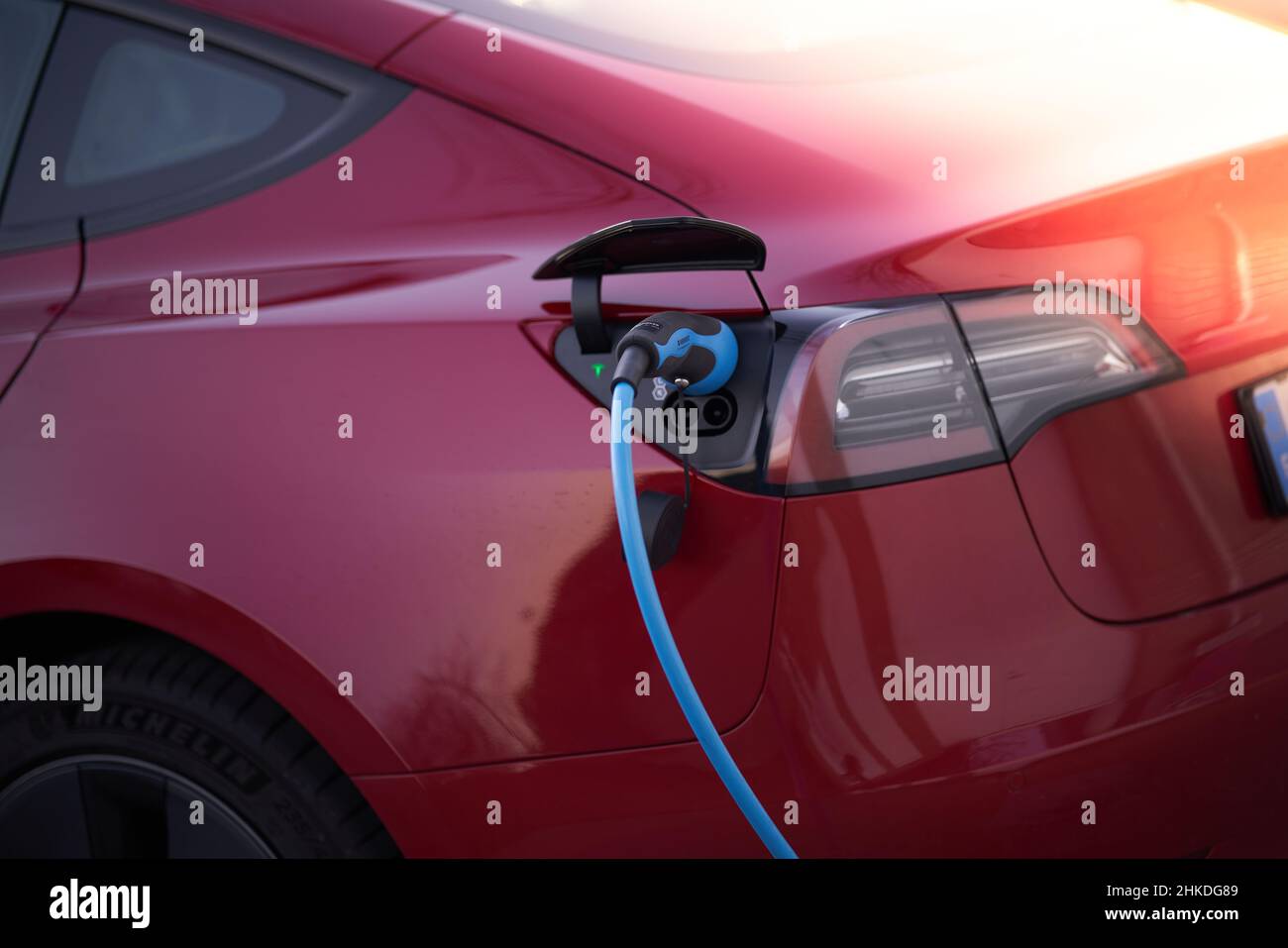 Modern red electric vehicle at the time of charging connected to charging station. Stock Photo