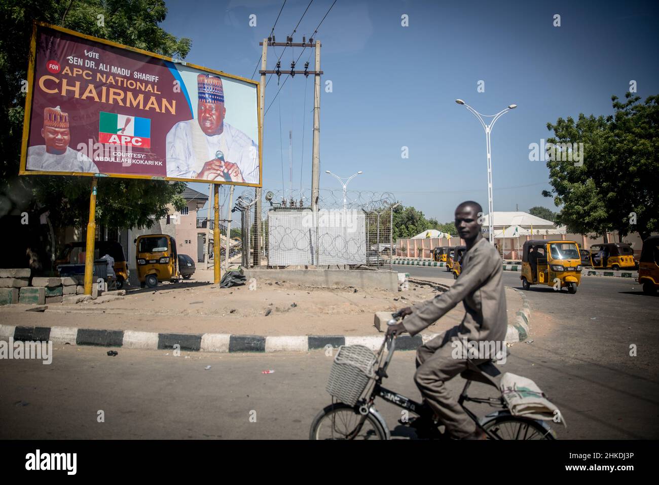 A man cycles past an election billboard in Maiduguri, the capital of Borno State.Islamic militant group Boko Haram, and more recently a faction called ISWAP, have been waging an insurgency in northeast Nigeria for more than a decade. Stock Photo