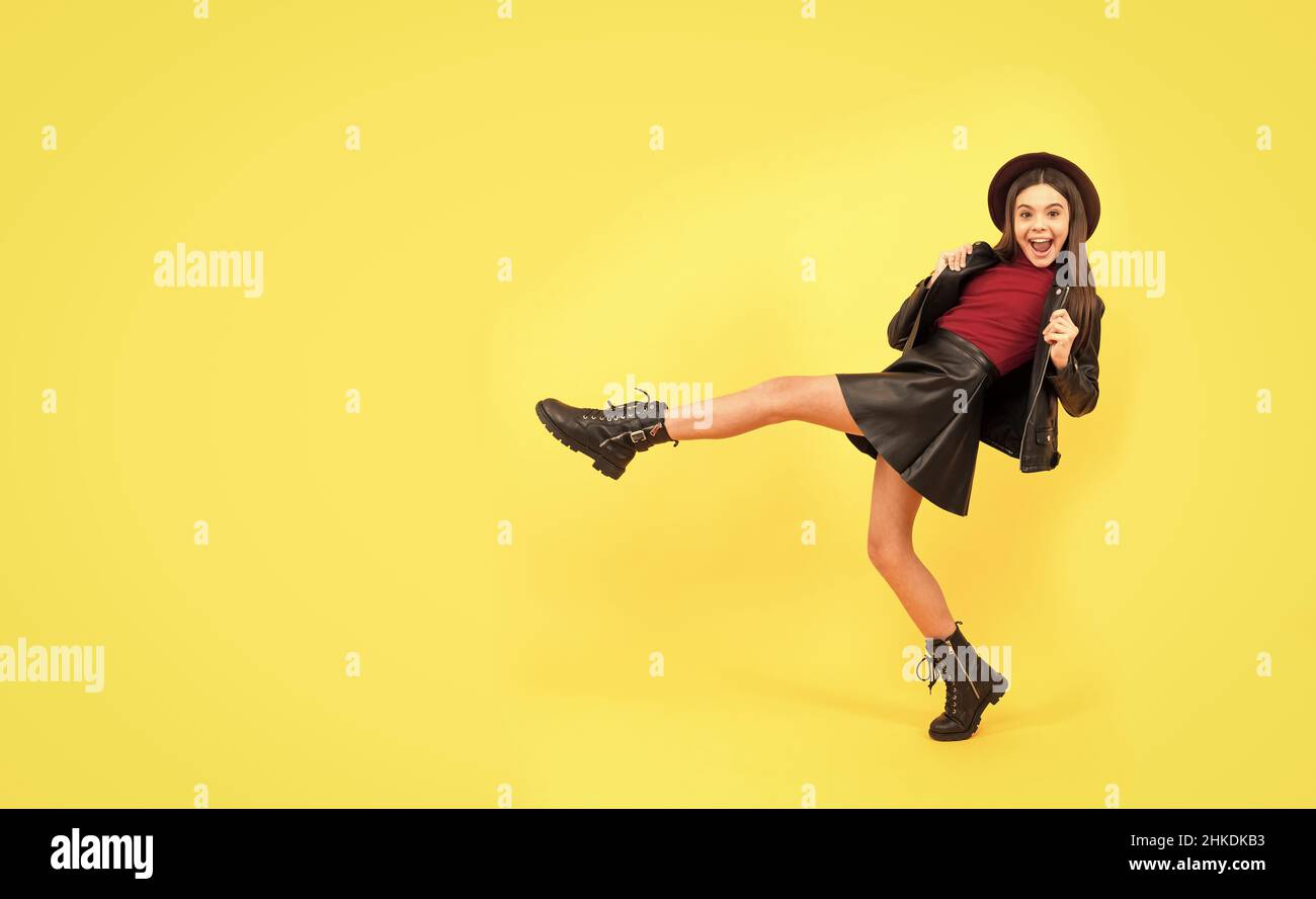 happy teen girl in hat and leather clothes making wide step forward, copy space, having fun Stock Photo