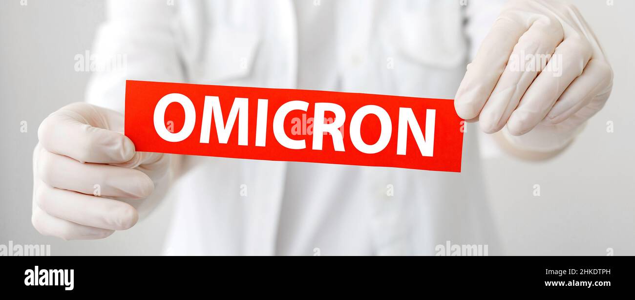Omicron red warning sign with text new Omicron variant covid 19 in doctor hands in white coat and gloves. Long web banner Stock Photo