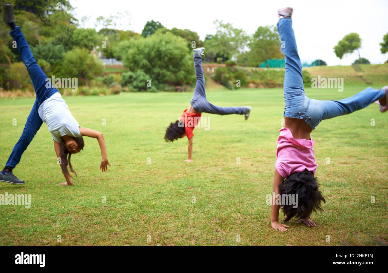 Cartwheel fun. Three young children doing handstands in the park. Stock Photo