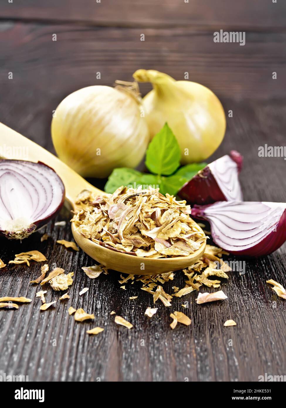 Dried onion flakes in a spoon, purple and yellow onions, basil on wooden board background Stock Photo