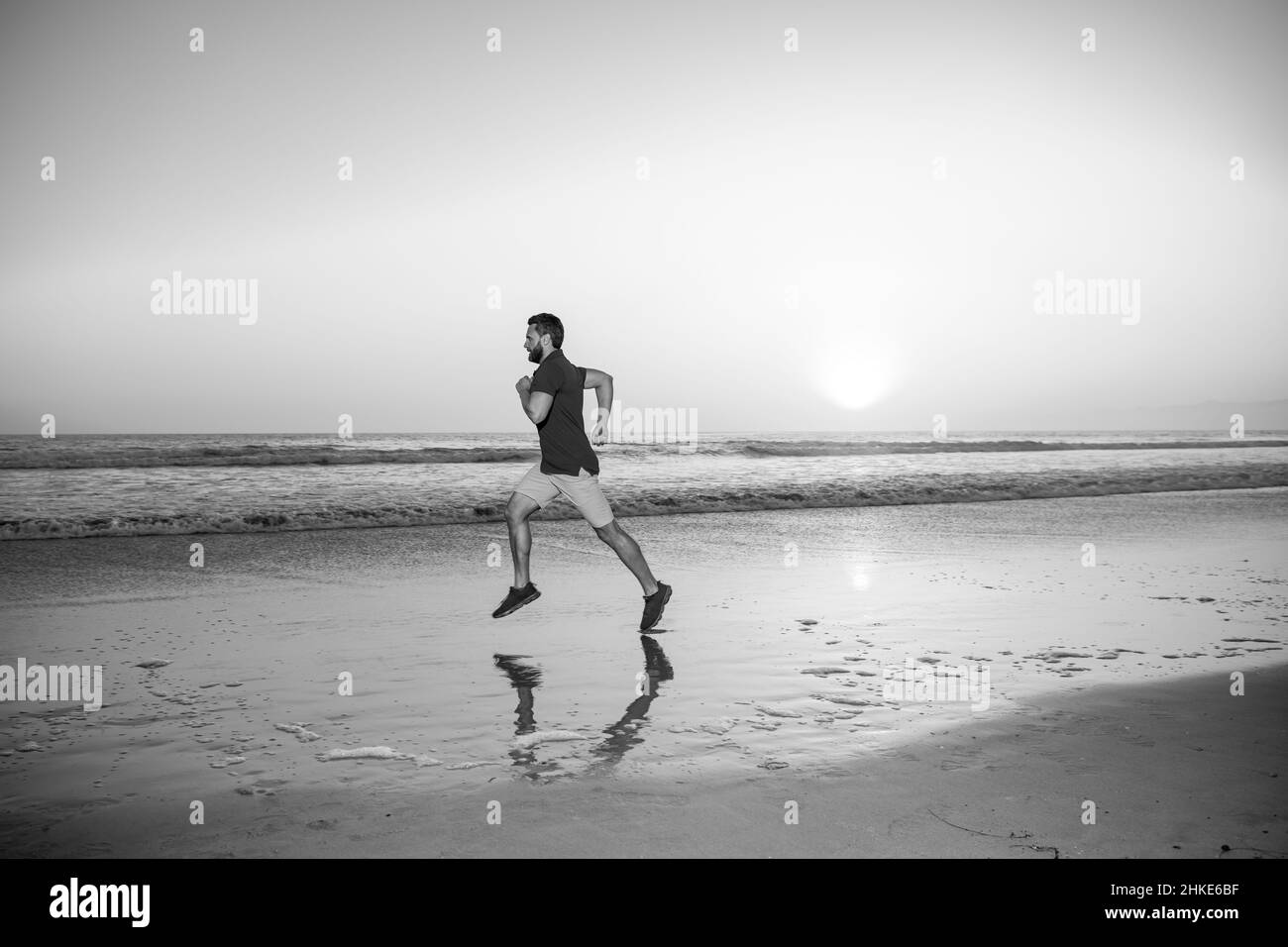 Man running on tropical beach at sunset. Full length of healthy man running and sprinting outdoors. Male runner. Sport and healthy lifestyle. Stock Photo