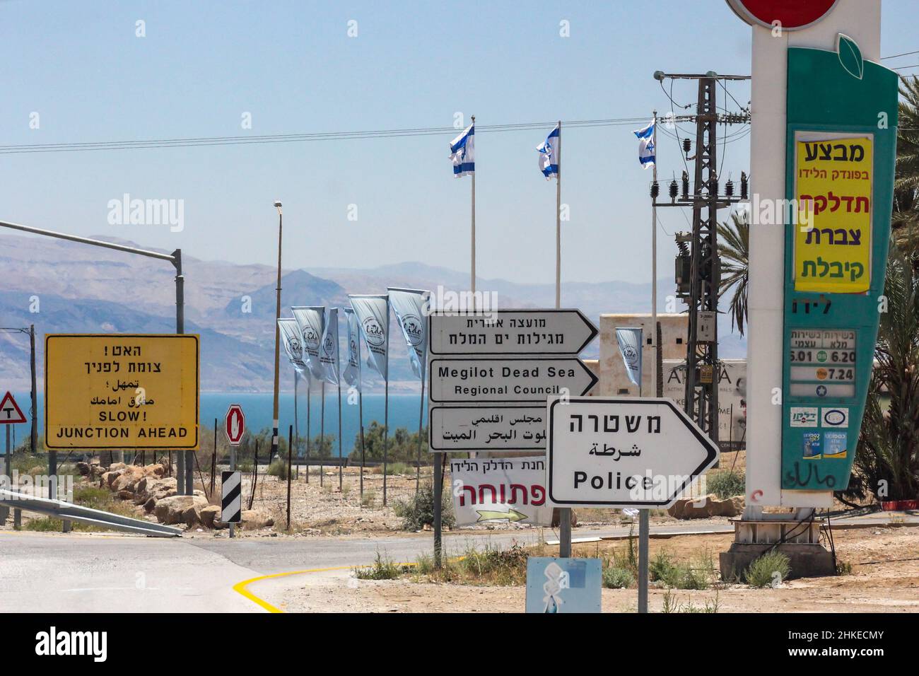 Israeli flags fly beyond trilingual signs written in Hebrew, Arabic and English directing travelers to various destinations near the Dead Sea. Stock Photo