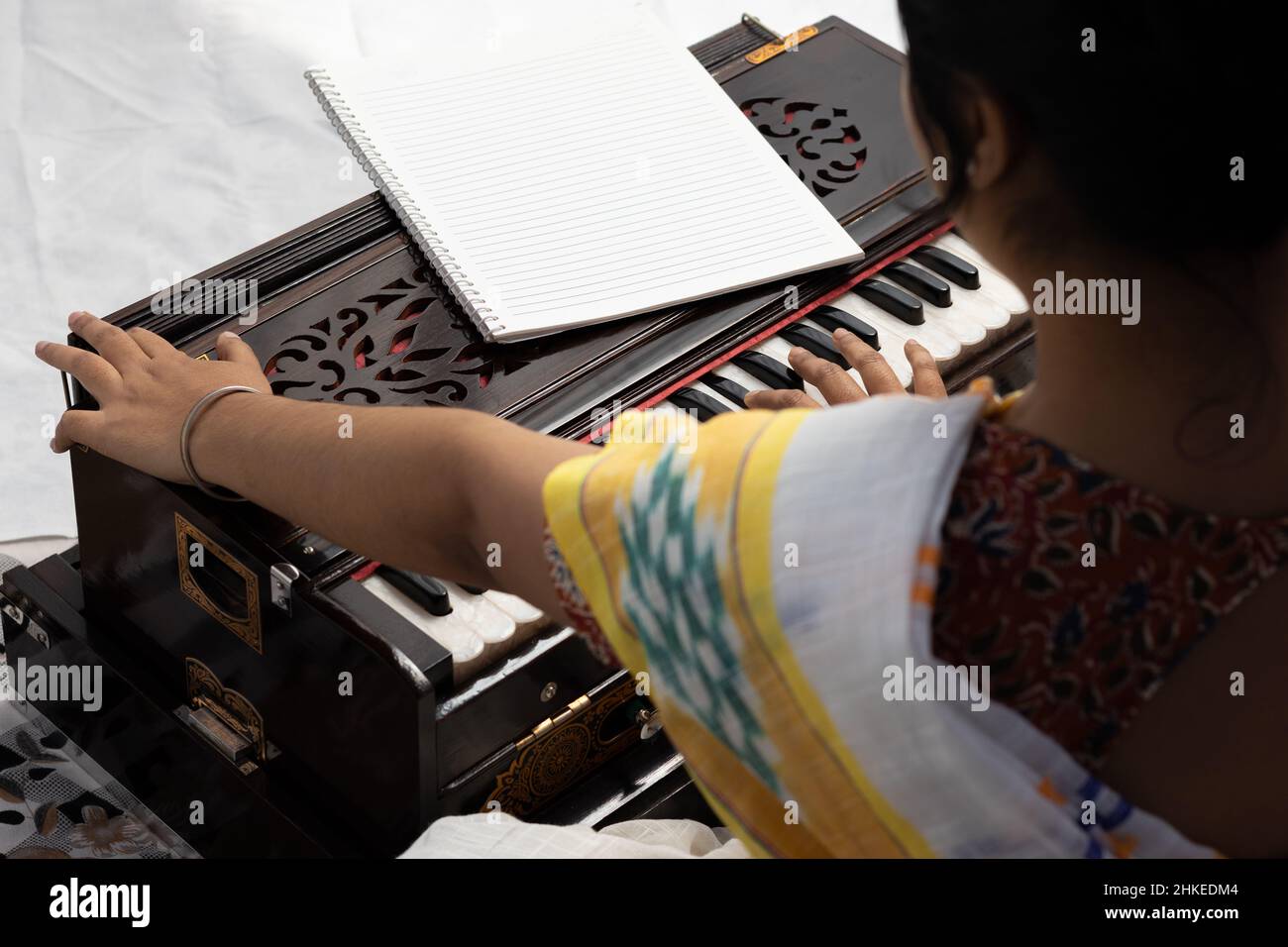 An Indian woman in saree singing and playing harmonium on white background with selective focus Stock Photo