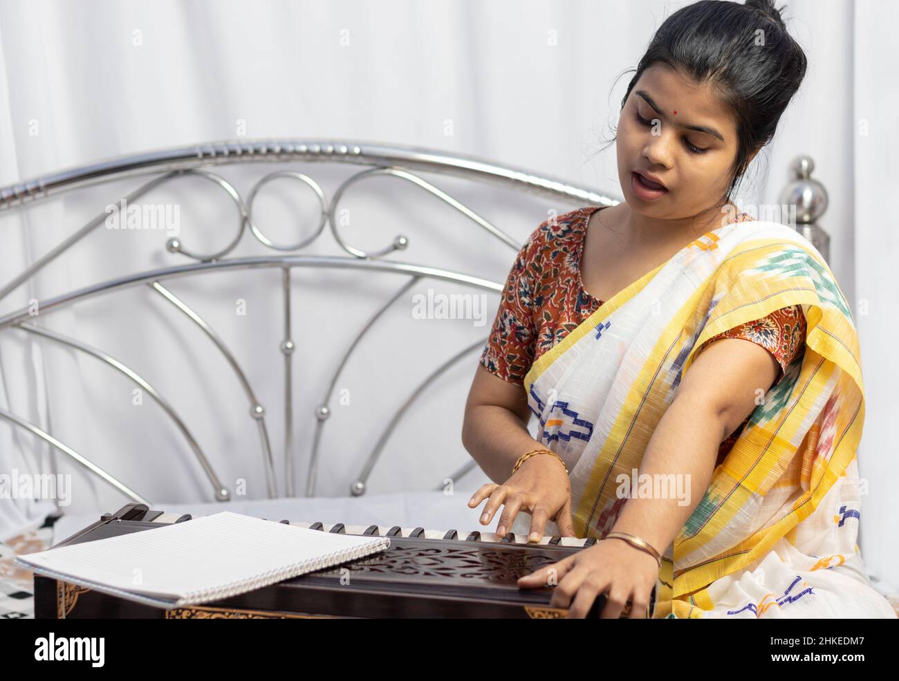 A beautiful Indian woman in saree singing and playing harmonium on white background Stock Photo