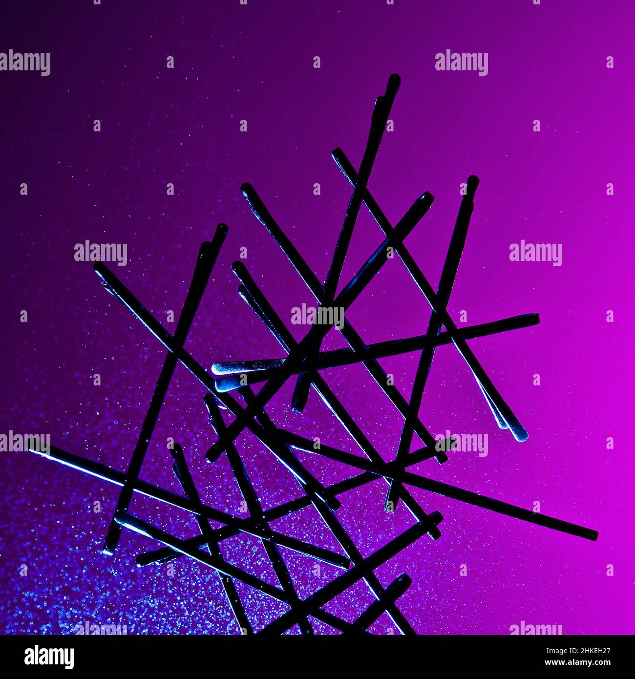 An abstract conceptual artful silhouette of bobby pins, backlit against a saturated purple and pink background with a glowing misted spray Stock Photo