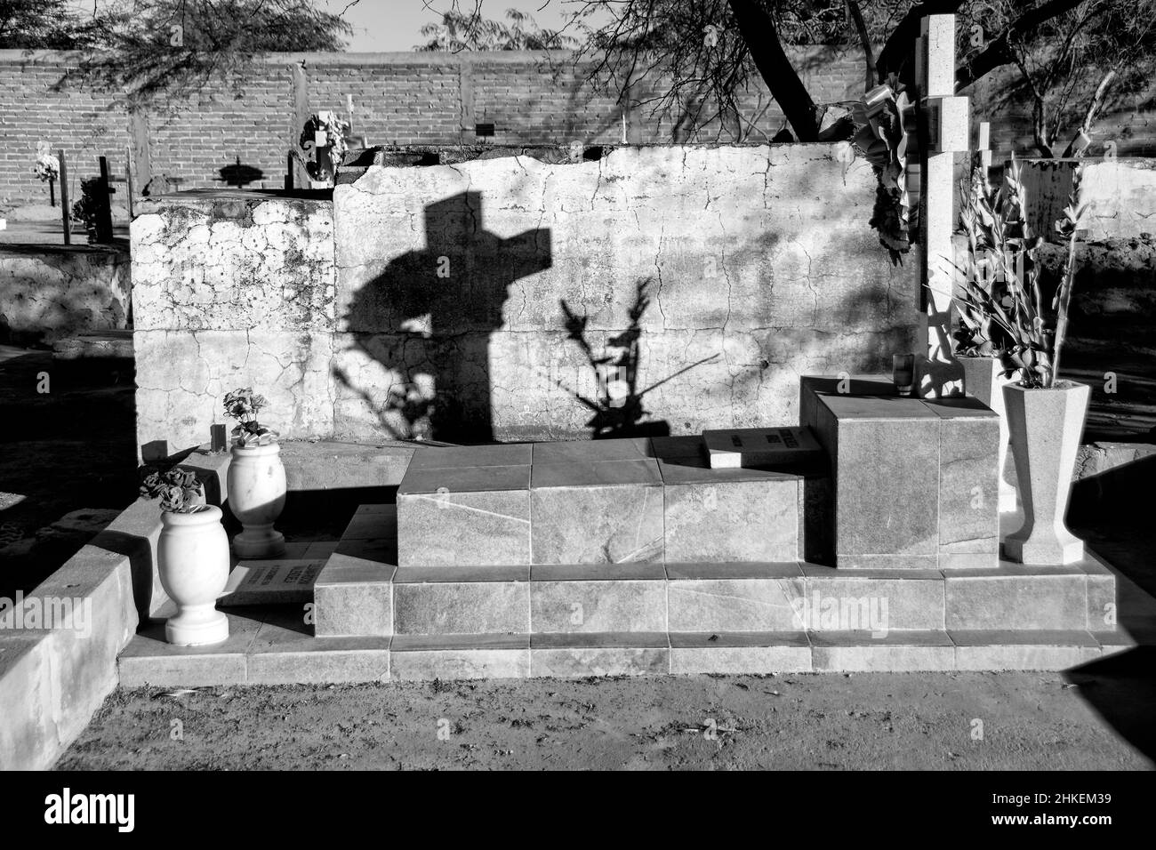 A black and white image of the shadow of a cross in a graveyard appearing on a wooden fence next to it. Puerto Penasco, Mexico. Stock Photo
