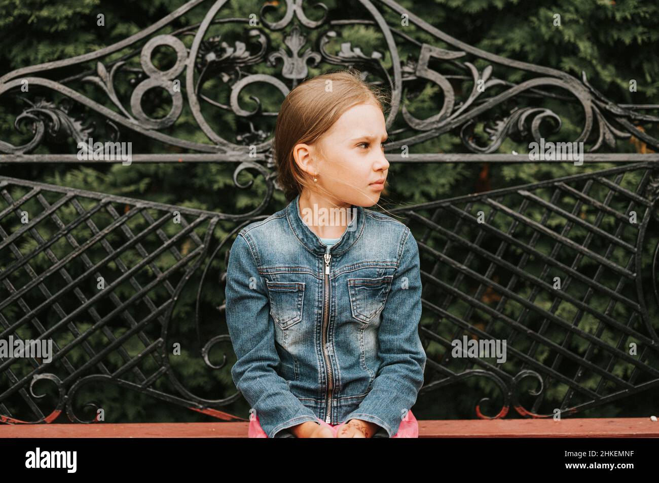 thoughtful scowl candid eight year old kid girl sits on bench and observe nature. prepubertal age of children and their lives, mind psychology and men Stock Photo