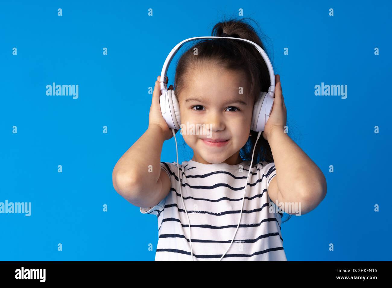 Little girl child wear headphones listen to music over blue background
