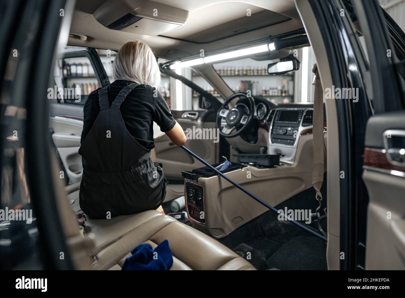 Worker woman vacuum cleaning dust interior inside car in car wash Stock